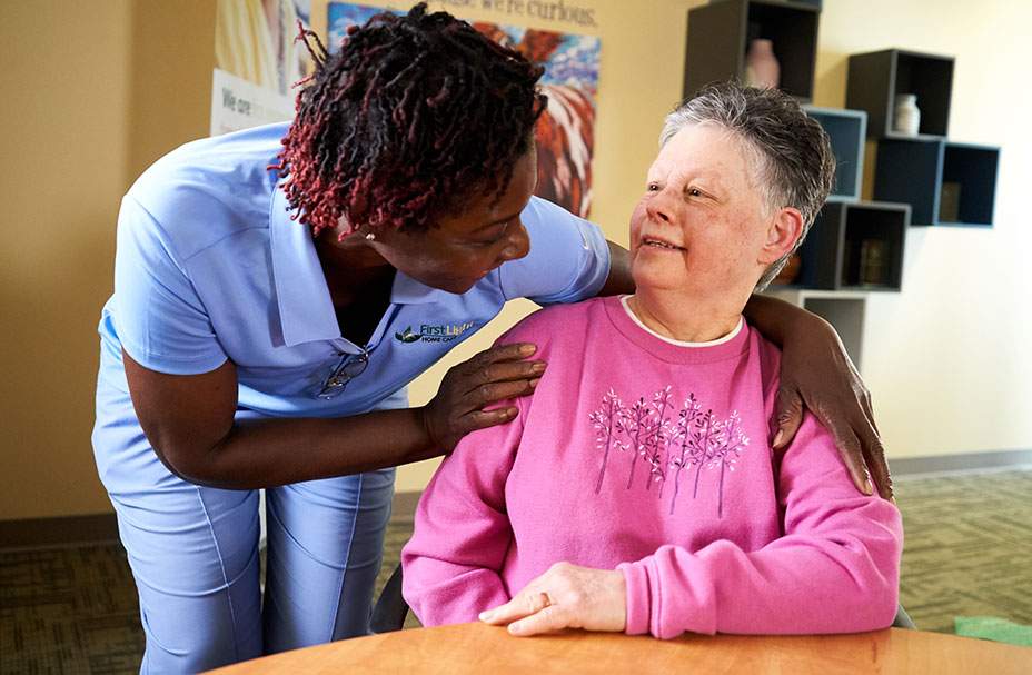 Caretaking woman leaning over shoulder sitting at table