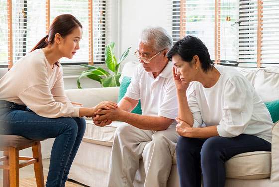 A woman hold's her father's hand, while her mom looks on