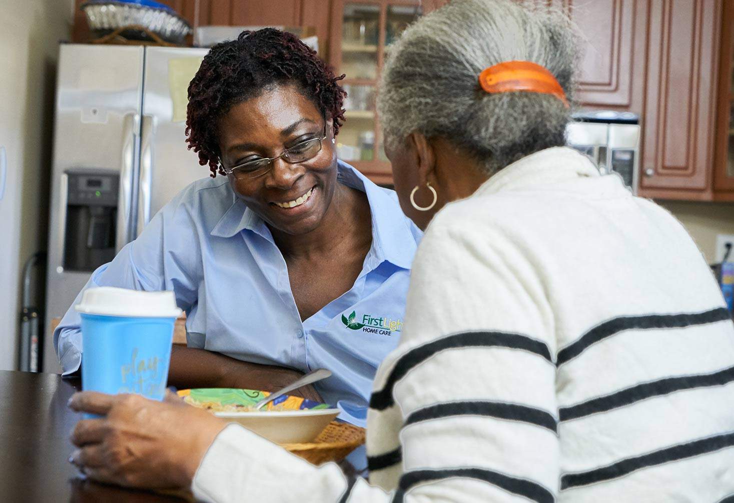 A caregiver sites at a table with a client who is eating lunch