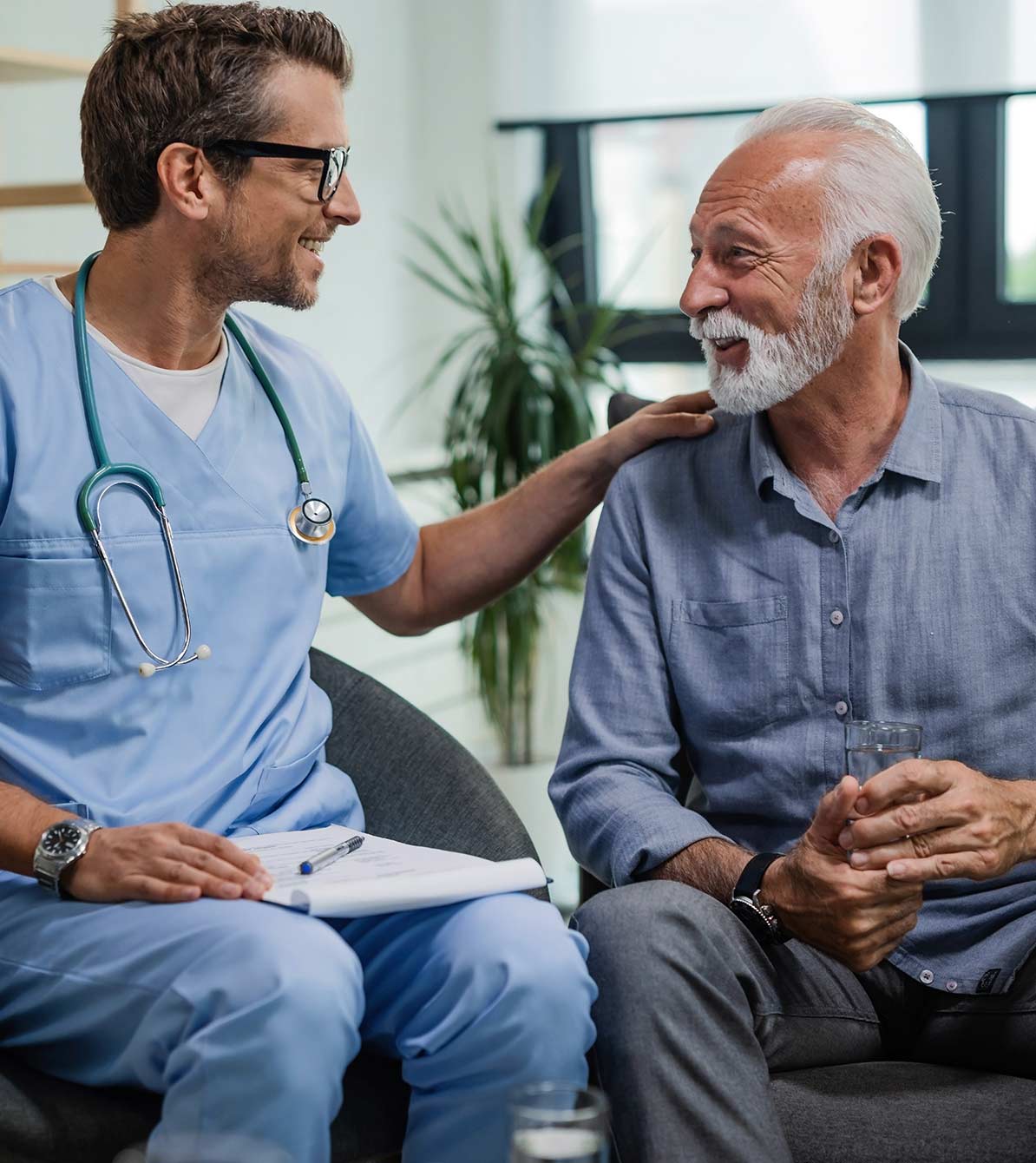 A nurse meets with a client. The nurse has a clipboard on his lap